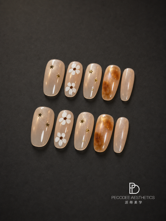 Amber star bloom press-on nails set, nude and amber tips with stars and floral accents.