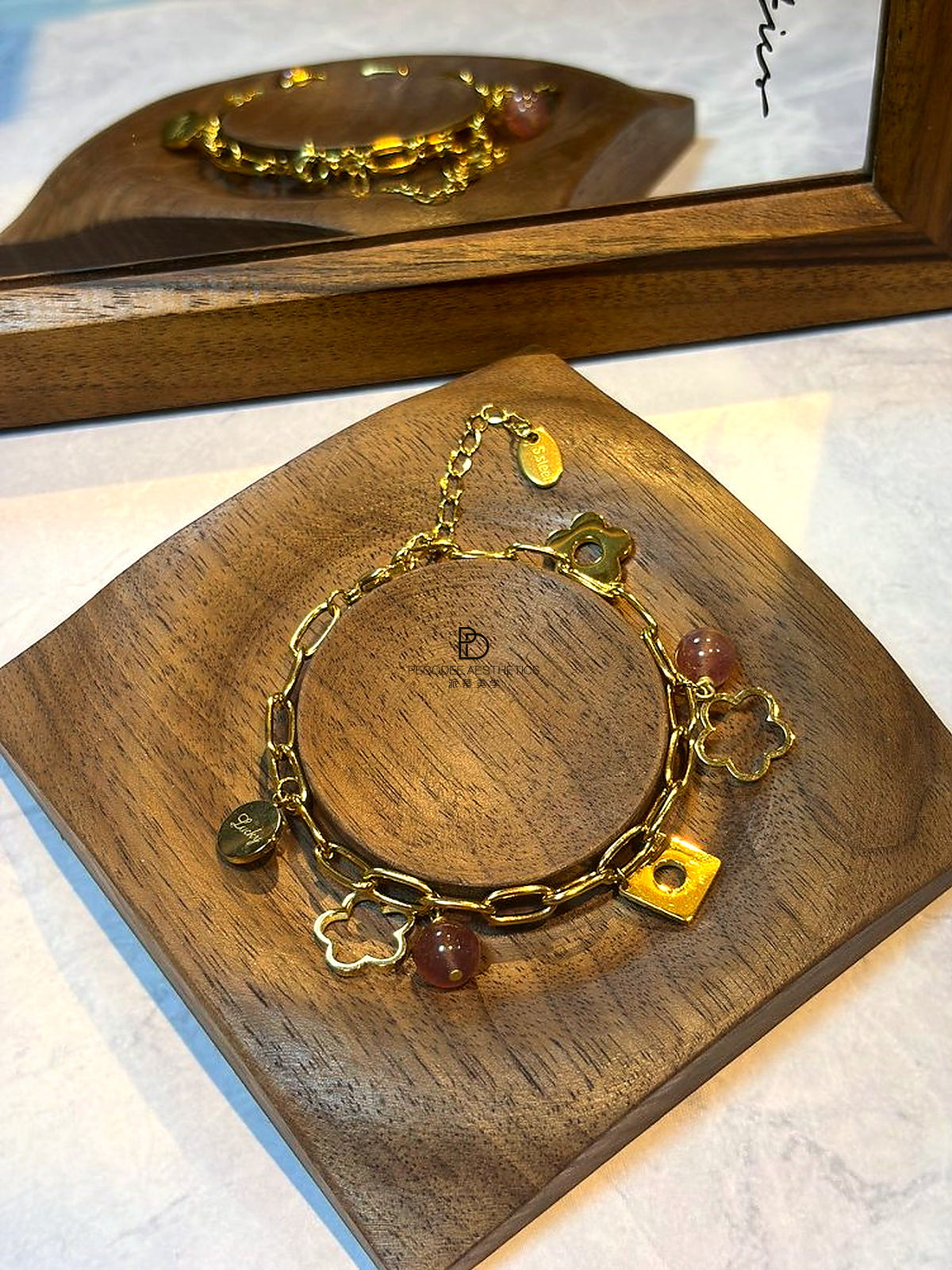 Gold chain bracelet with berry beads, clover and heart charms, and square tag clasp
