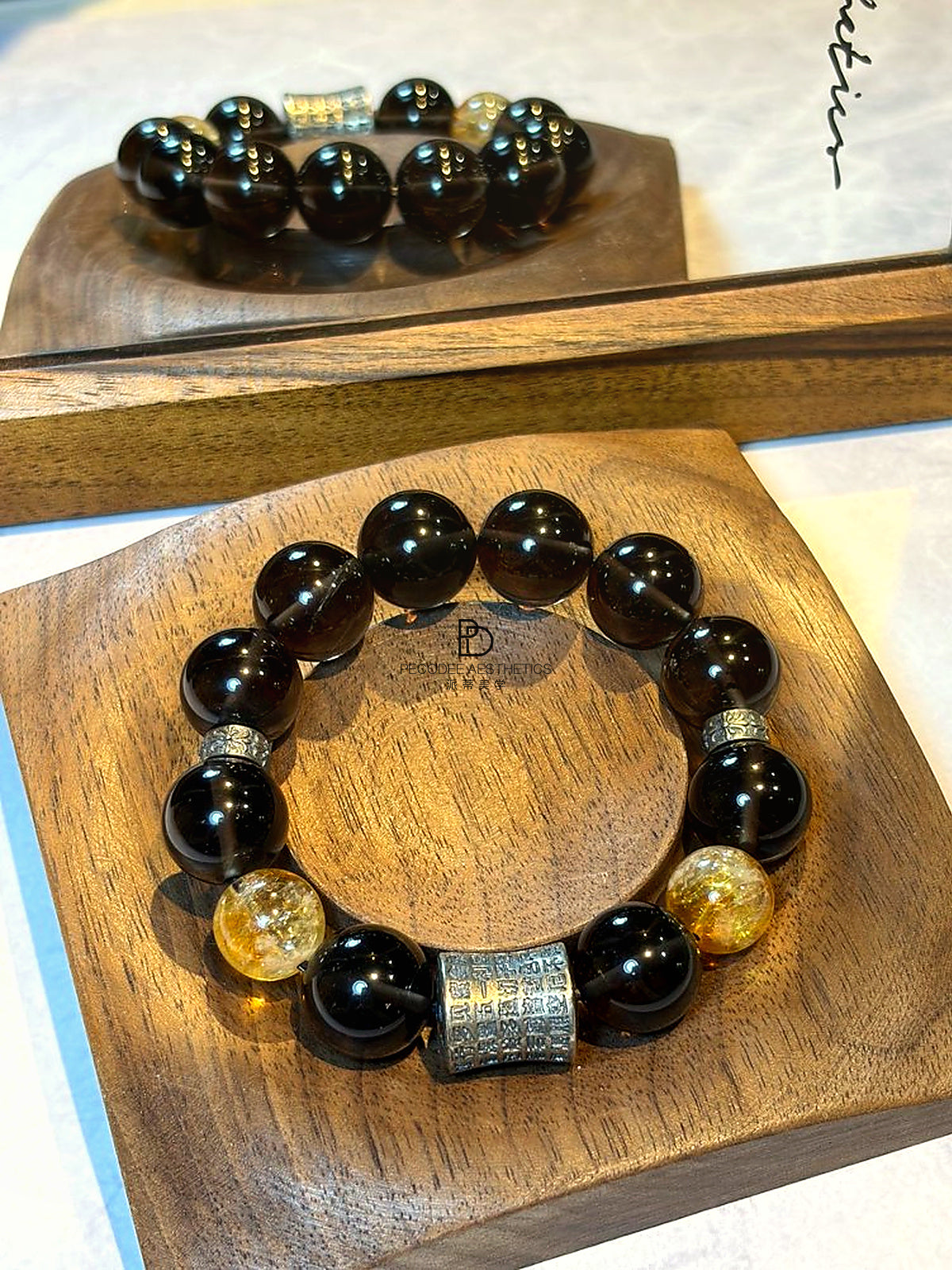 Beaded bracelet with dark beads, golden round beads, and a silver-toned rectangular charm