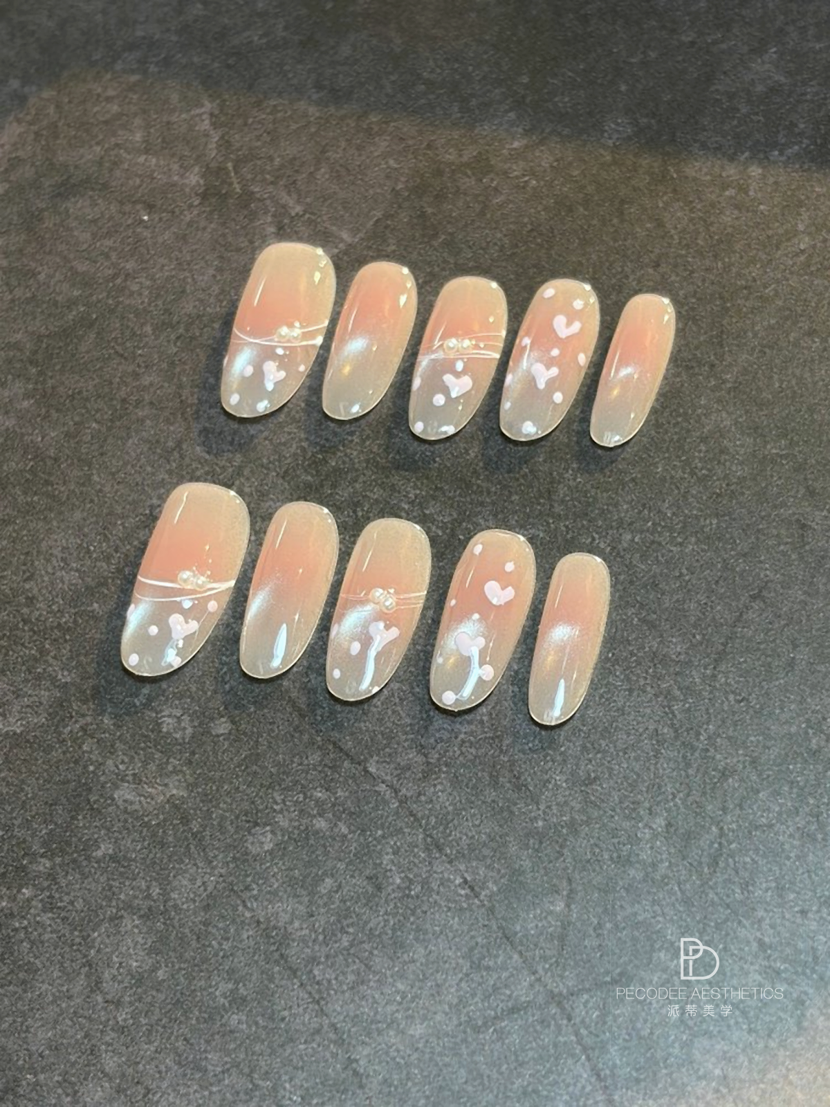 Peach press-on nails with white heart and floral accents, glossy almond shape