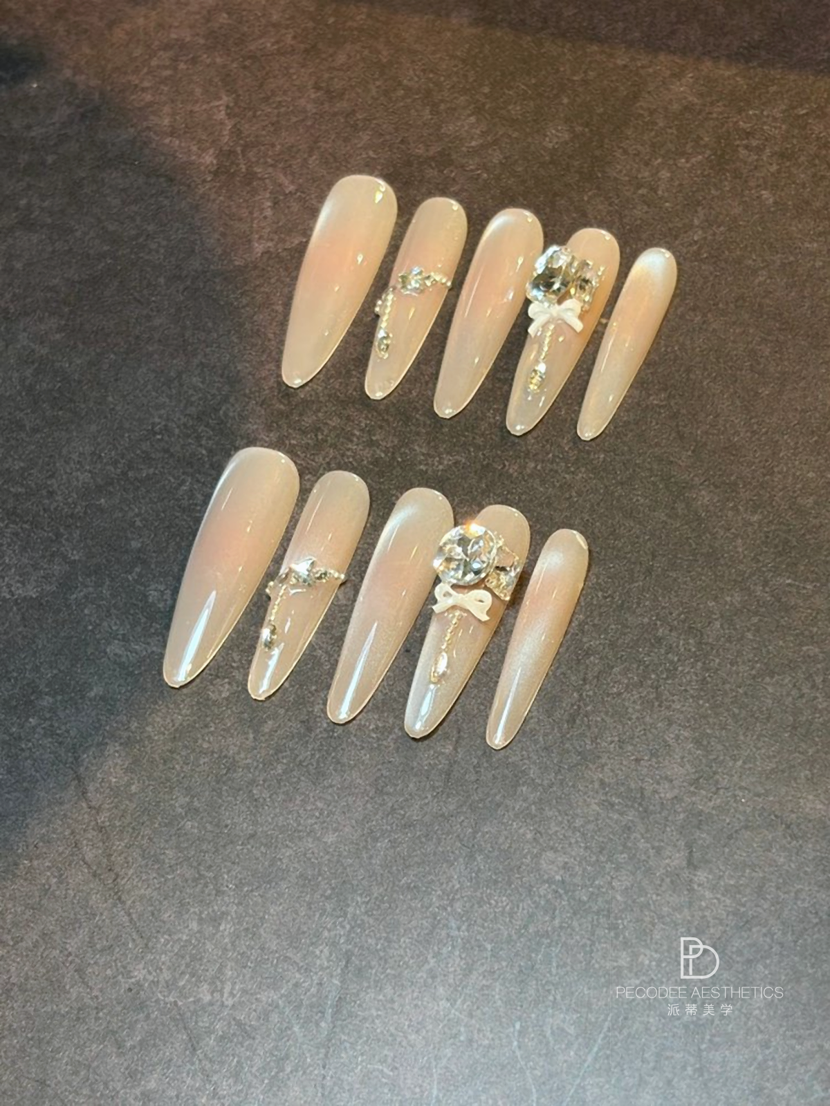 Satin gift bow nail art with rhinestone accents on pale beige long nails
