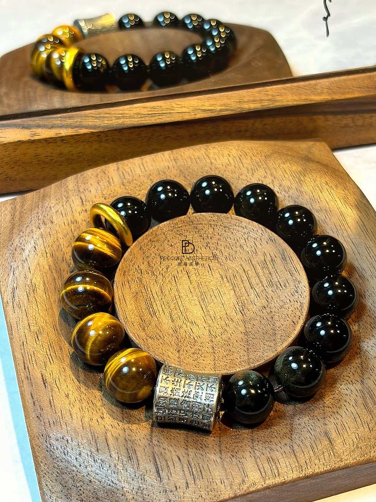 Beaded bracelet with black round beads and gold spacer beads, with a square patterned charm centerpiece.
