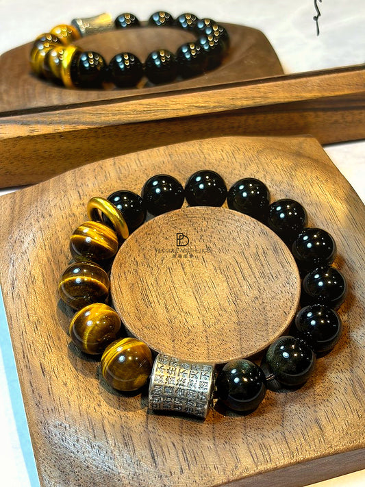 Beaded bracelet with black round beads and gold spacer beads, with a square patterned charm centerpiece.